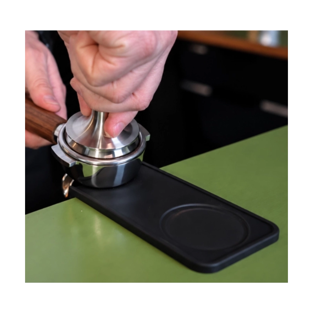 Kaffeemacher schmale Tamping-Matte in Schwarz beim Verdichten von Kaffeemehl im Siebträger mit einem Edelstahl-Tamper
