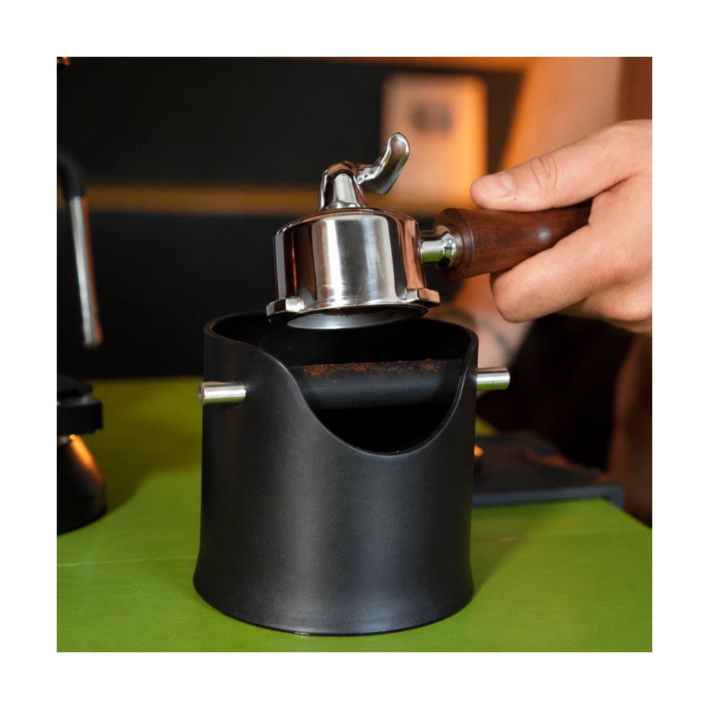 Abschlagbehälter Knock Box in Schwarz bei der Anwendung mit einem Siebträger mit Holzgriff zum Ausklopfen des Kaffeesatzes